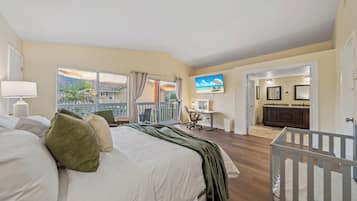 Ein Schlafzimmer mit einem großen Bett, einem Schreibtisch, einem Babybett und einem Balkon mit Blick auf den Strand.
