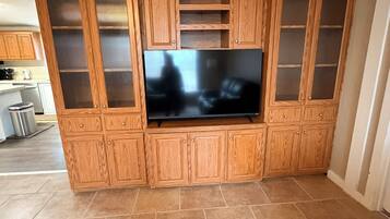 A kitchen with a built-in entertainment center, a large flat-screen TV, and a tiled floor.