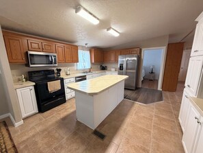 A modern kitchen with wooden cabinets, a stainless steel refrigerator, and a large island.