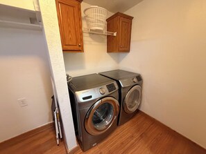 A laundry room with two stacked washers and dryers, wooden cabinets, and a white laundry basket on the wall.