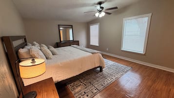 A bedroom with a bed, bedside table, lamp, ceiling fan, windows, and a rug.