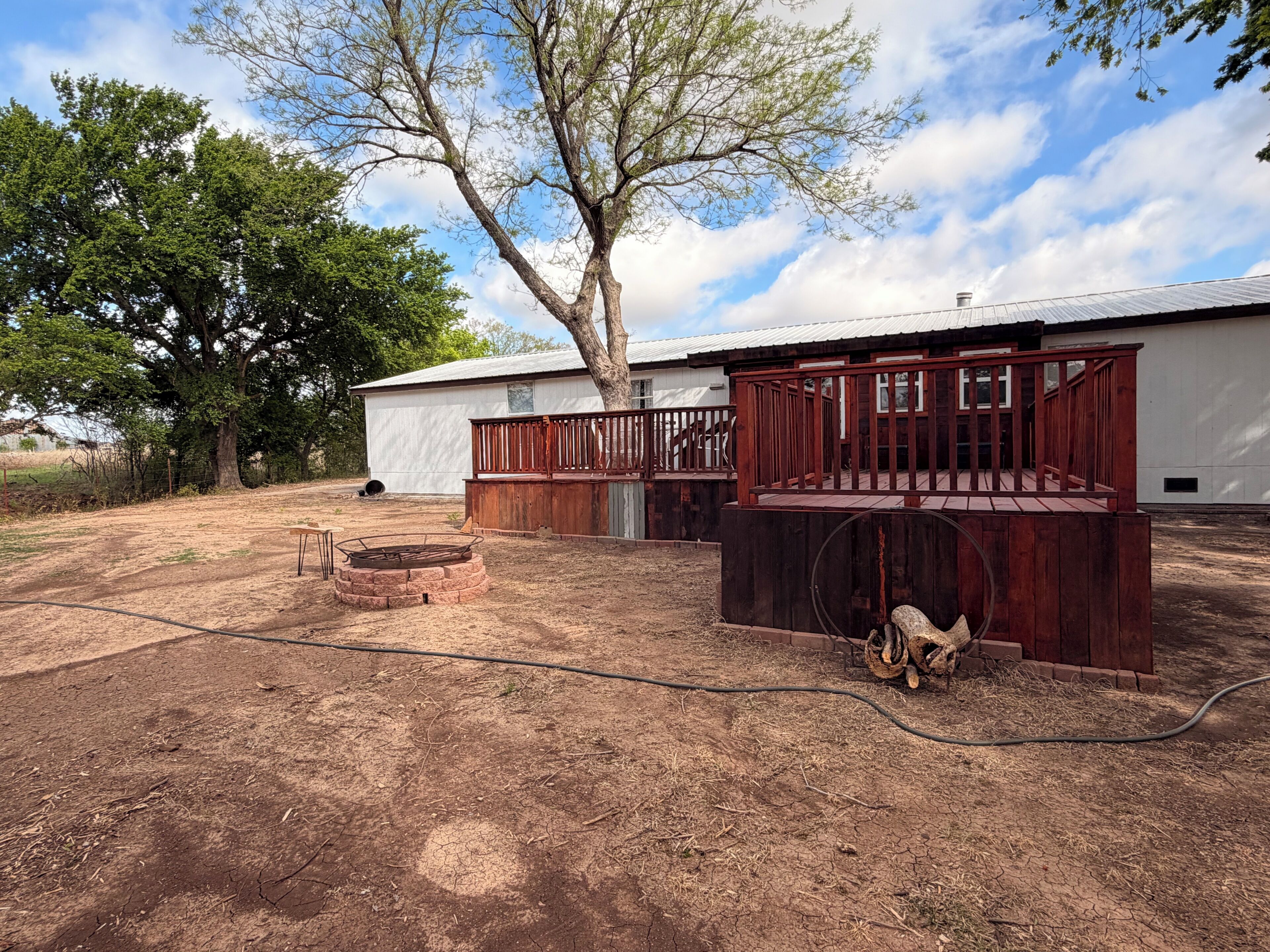 A fenced outdoor area with a fire pit, a wooden deck, and a building with a metal roof.