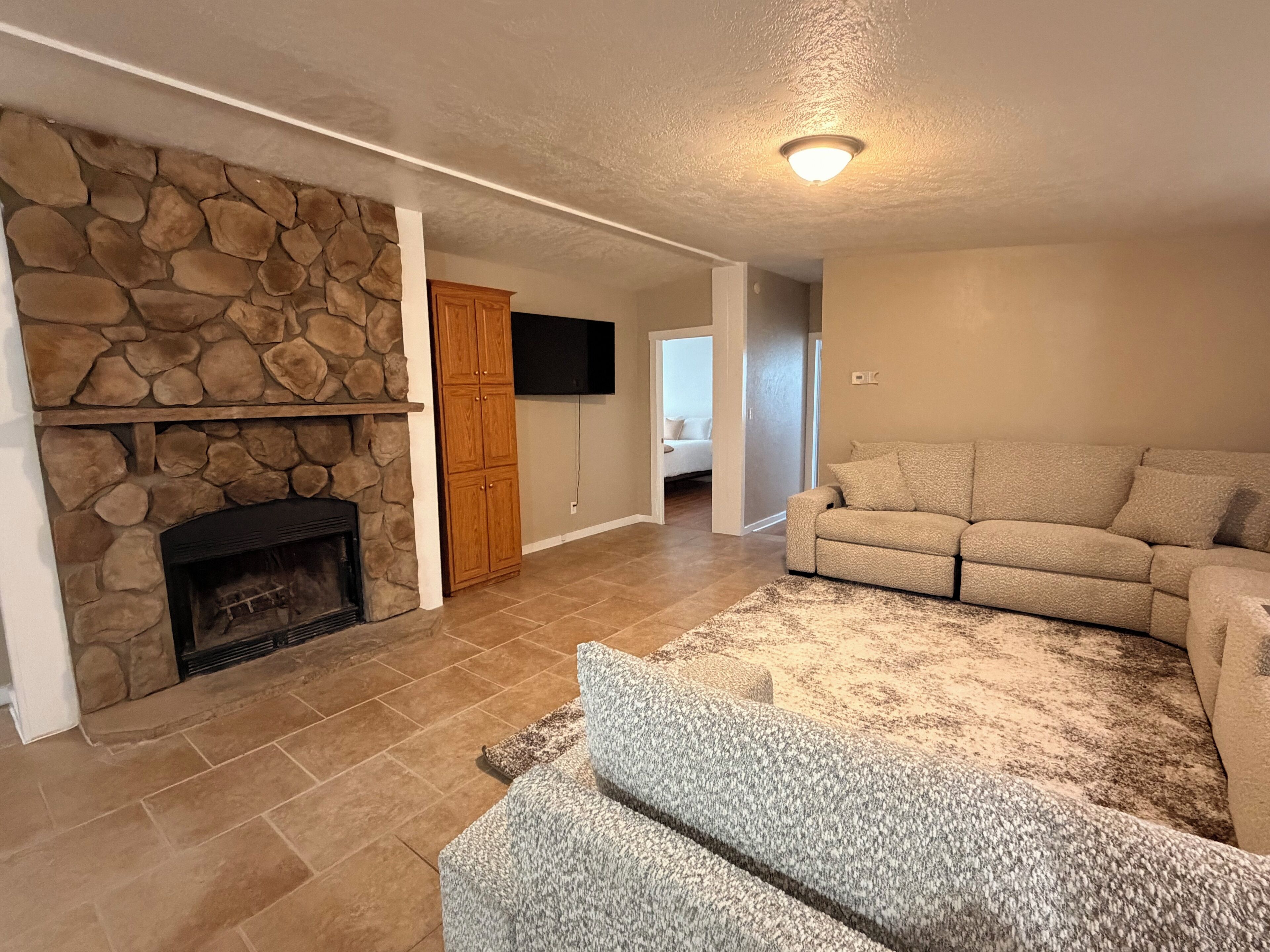 A living room with a stone fireplace, a beige sofa, and a flat-screen TV mounted on the wall.