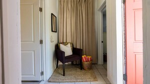 A hallway with a door, a chair with cushions, a basket with striped items, and a curtain. - El Apartemento | Cozy 1BR Cottage with Private Deck Near Ybor City, Armature Works & Downtown Tampa (Tampa)