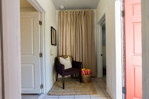 Un pasillo con una puerta, una silla con cojines, una cesta con objetos a rayas y una cortina.