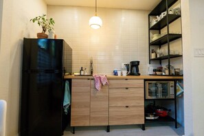 Una cocina compacta con un refrigerador negro, armarios de madera, una encimera con cafetera y microondas.