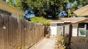 A backyard with a wooden fence, a covered patio area, and a garage. - El Apartemento | Cozy 1BR Cottage with Private Deck Near Ybor City, Armature Works & Downtown Tampa (Tampa)