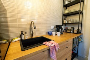 A kitchen with a sink, a coffee maker, and neatly organized shelves. - El Apartemento | Cozy 1BR Cottage with Private Deck Near Ybor City, Armature Works & Downtown Tampa (Tampa)