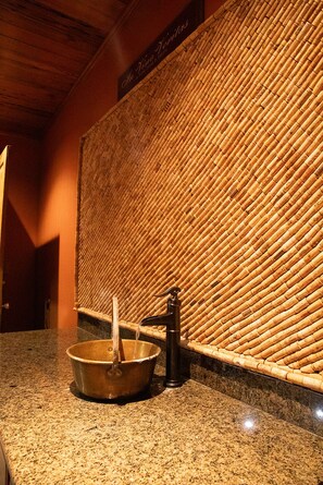 Un baño con pared de bambú, encimera de granito, lavabo de metal y grifo.