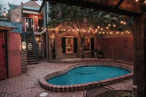 Una piscina de ladrillo con un patio circundante, una escalera y luces colgantes.