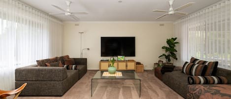 Una sala de estar con dos sofás, una mesa de centro, un televisor y ventiladores de techo.