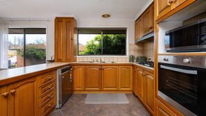 A kitchen with wooden cabinets, a dishwasher, a stove, and a window with a view of greenery. - Courtside Cabana | Pool, Basketball & Pet Friendly (Rosebud)