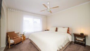 Una camera da letto con un letto grande, una sedia, un comodino con lampada, una ventola a soffitto e una finestra con tende.