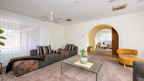 A modern living room with a sofa, armchairs, a glass coffee table, and a ceiling fan. - Courtside Cabana | Pool, Basketball & Pet Friendly (Rosebud)
