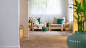 A living room with two armchairs, a small ottoman, a side table, and a large window with sheer curtains. - Courtside Cabana | Pool, Basketball & Pet Friendly (Rosebud)