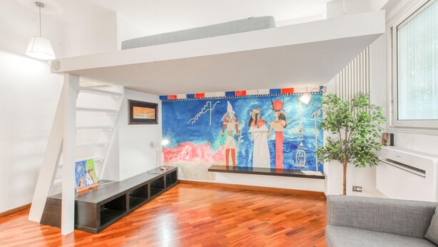 A modern living room with a wooden floor, a grey sofa, a staircase, and a wall mural. - Gorgeous apartment in Genova with WiFi (Genova)