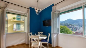 Ein Essbereich mit Tisch und Stühlen, einer Kronleuchter, einem an der Wand montierten Fernseher und Blick auf eine Stadtansicht durch große Fenster.