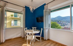 A dining area with a table and chairs, a chandelier, a TV mounted on the wall, and a view of a cityscape through large windows. - 1 bedroom amazing apartment in Rapallo (Rapallo)