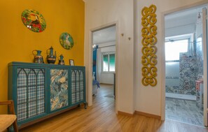 Ein Korridor mit Holzboden, einem blauen Schrank mit Blumenmuster und einer gelben Wand mit dekorativen Tellern.