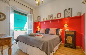 Une chambre à coucher comprenant un lit, des tables de chevet, une commode, un mur d’accent rouge et des œuvres d’art.