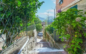 A narrow alleyway with a car parked on the right, flanked by lush greenery and a building with a visible window. - 1 bedroom amazing apartment in Rapallo (Rapallo)