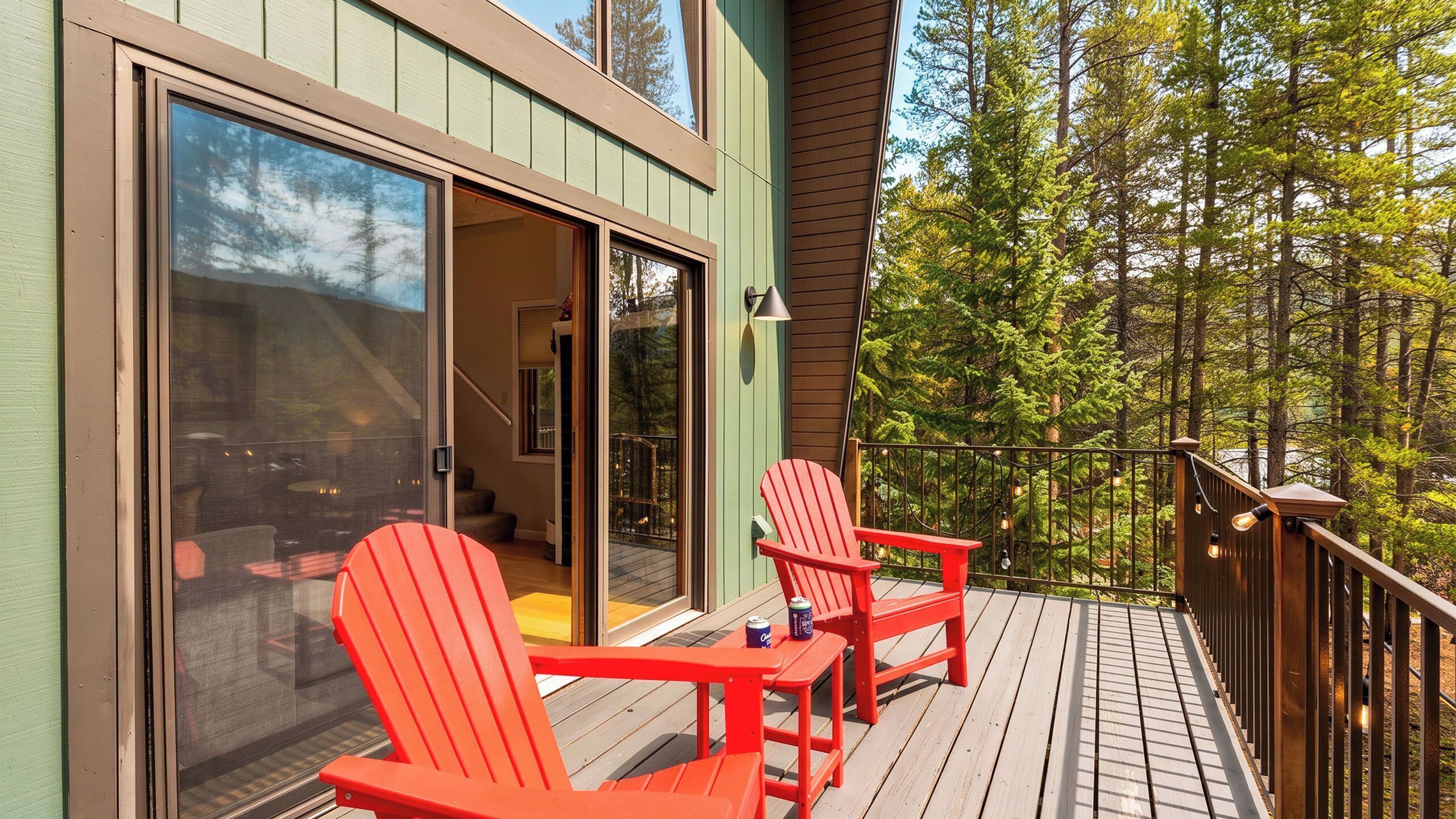 A deck with two red chairs and a table, overlooking a forested area.