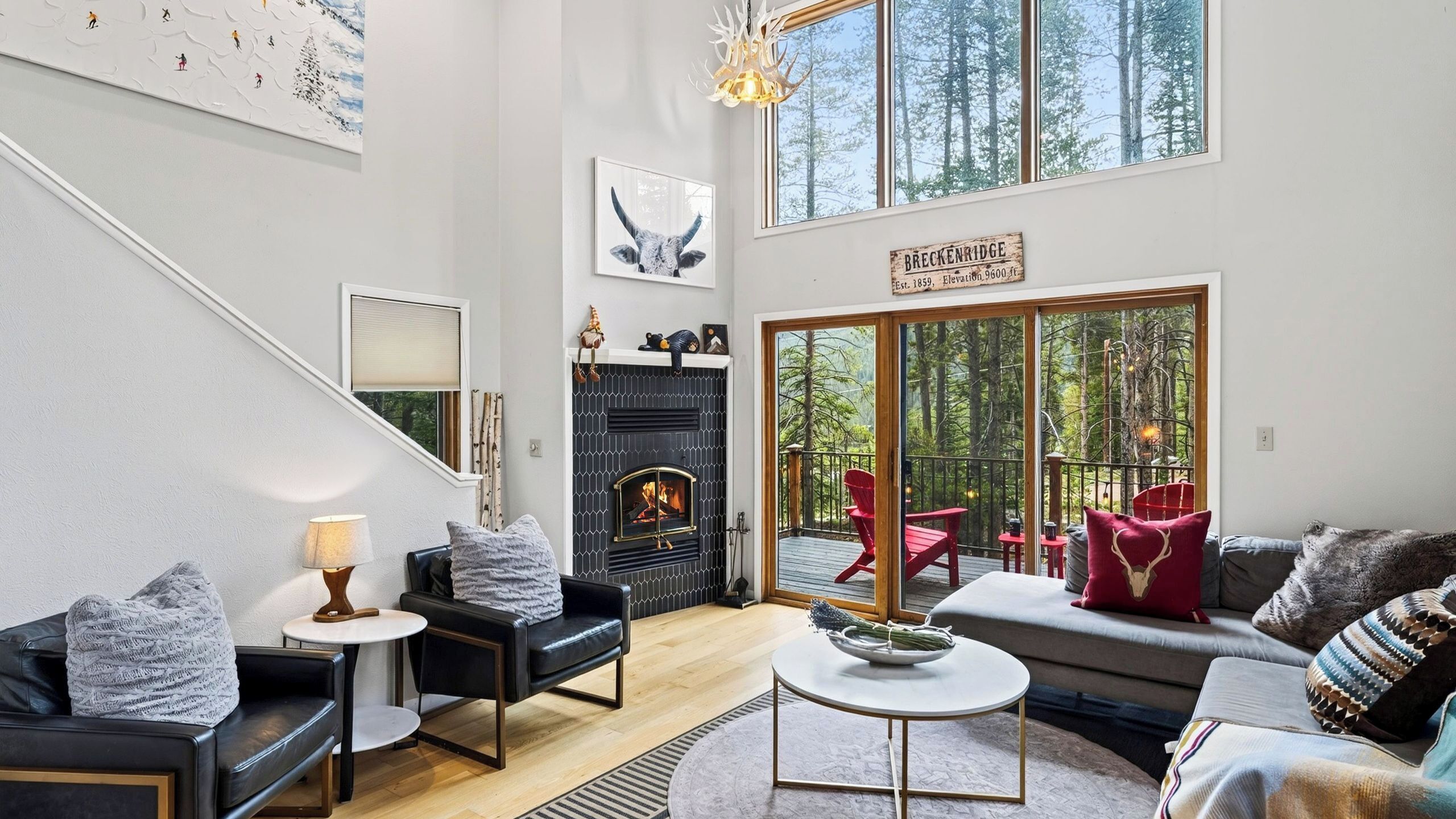 Una sala de estar moderna con chimenea, asientos y un ventanal grande con vistas a un bosque.