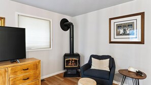 A living room with a television, a wooden cabinet, a blue armchair, a small round table, and a black wood-burning stove. - Pitch & Pine by Avantstay Hot Tub + Ping Pong + Arcade + Loft Lounge Ski, Hike + Main Street (Breckenridge)