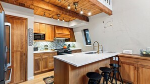 A modern kitchen with wooden cabinets, a central island with stools, a microwave, and a stove. - Pitch & Pine by Avantstay Hot Tub + Ping Pong + Arcade + Loft Lounge Ski, Hike + Main Street (Breckenridge)