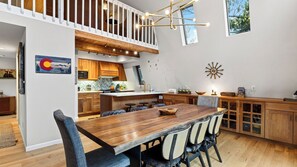 A modern kitchen with wooden cabinets, a dining area with a large wooden table, and a loft bedroom with a view. - Pitch & Pine by Avantstay Hot Tub + Ping Pong + Arcade + Loft Lounge Ski, Hike + Main Street (Breckenridge)