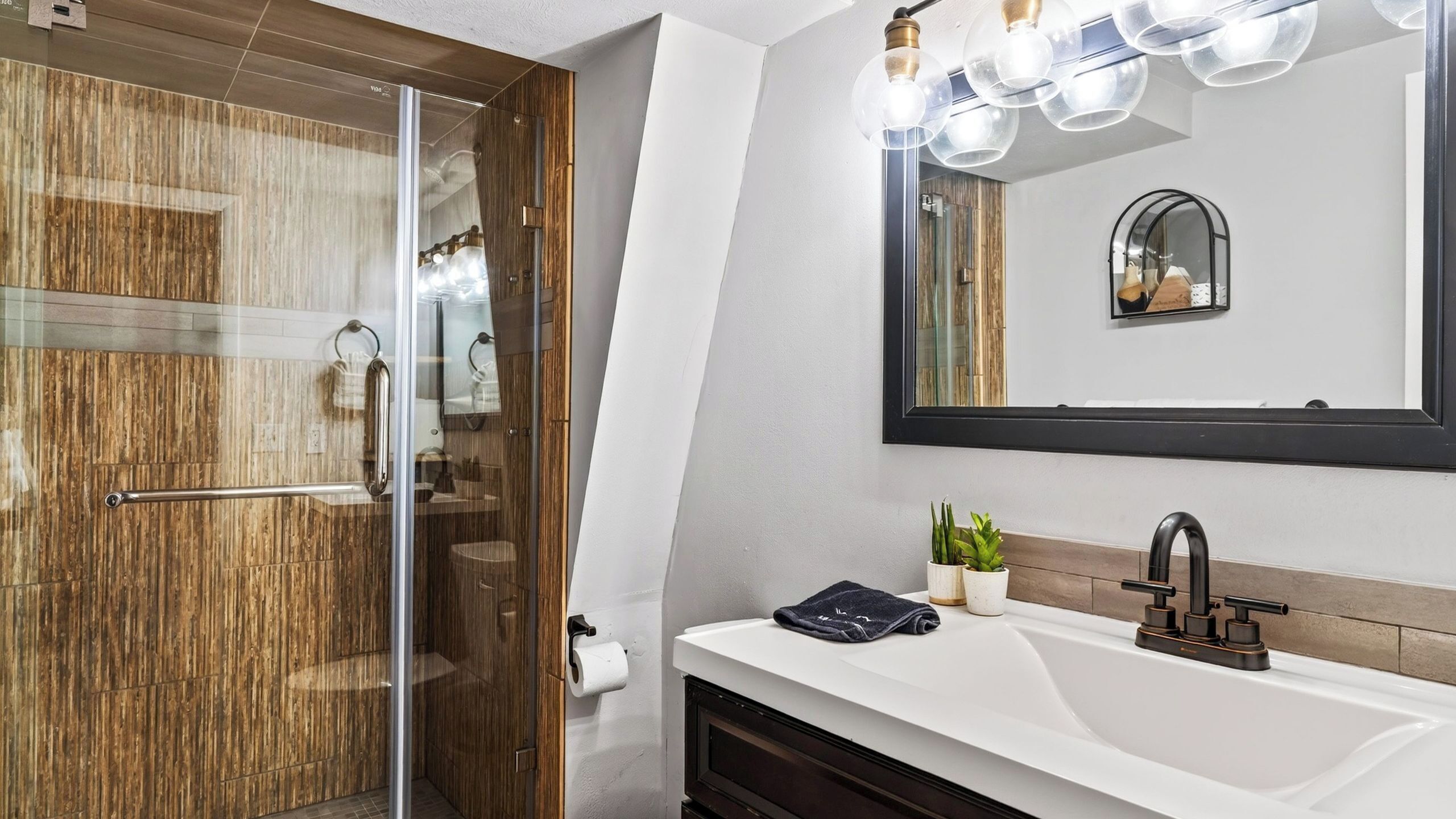 Een moderne badkamer met een douchecabine van glas, een witte wastafel met een zwarte kraan en een spiegel met een zwarte lijst.