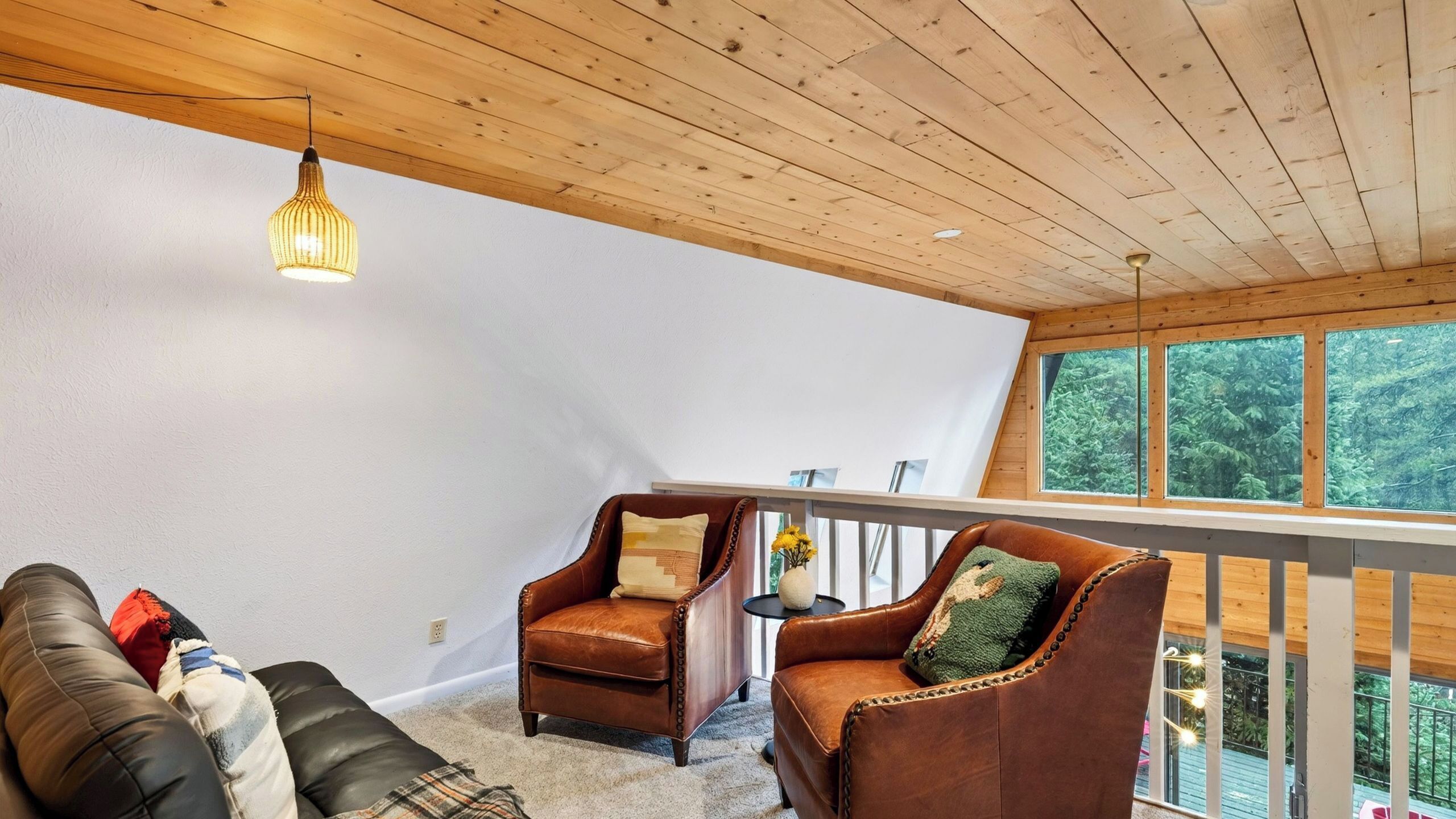 A cozy interior with a wooden ceiling, a leather sofa, two leather armchairs, and a small table with a vase of flowers.