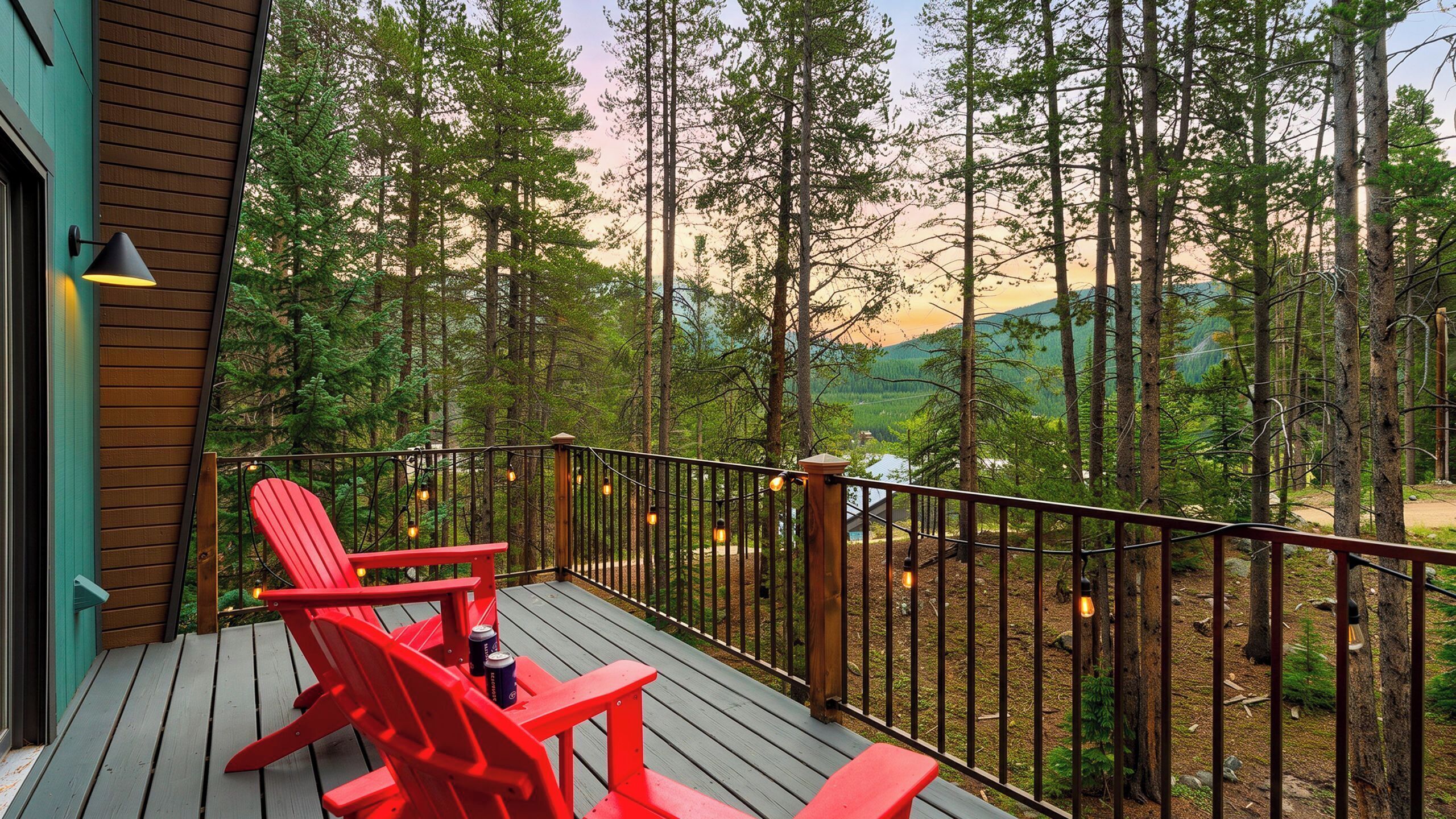 A wooden deck with red chairs and a table, overlooking a forested area with a mountain in the distance.