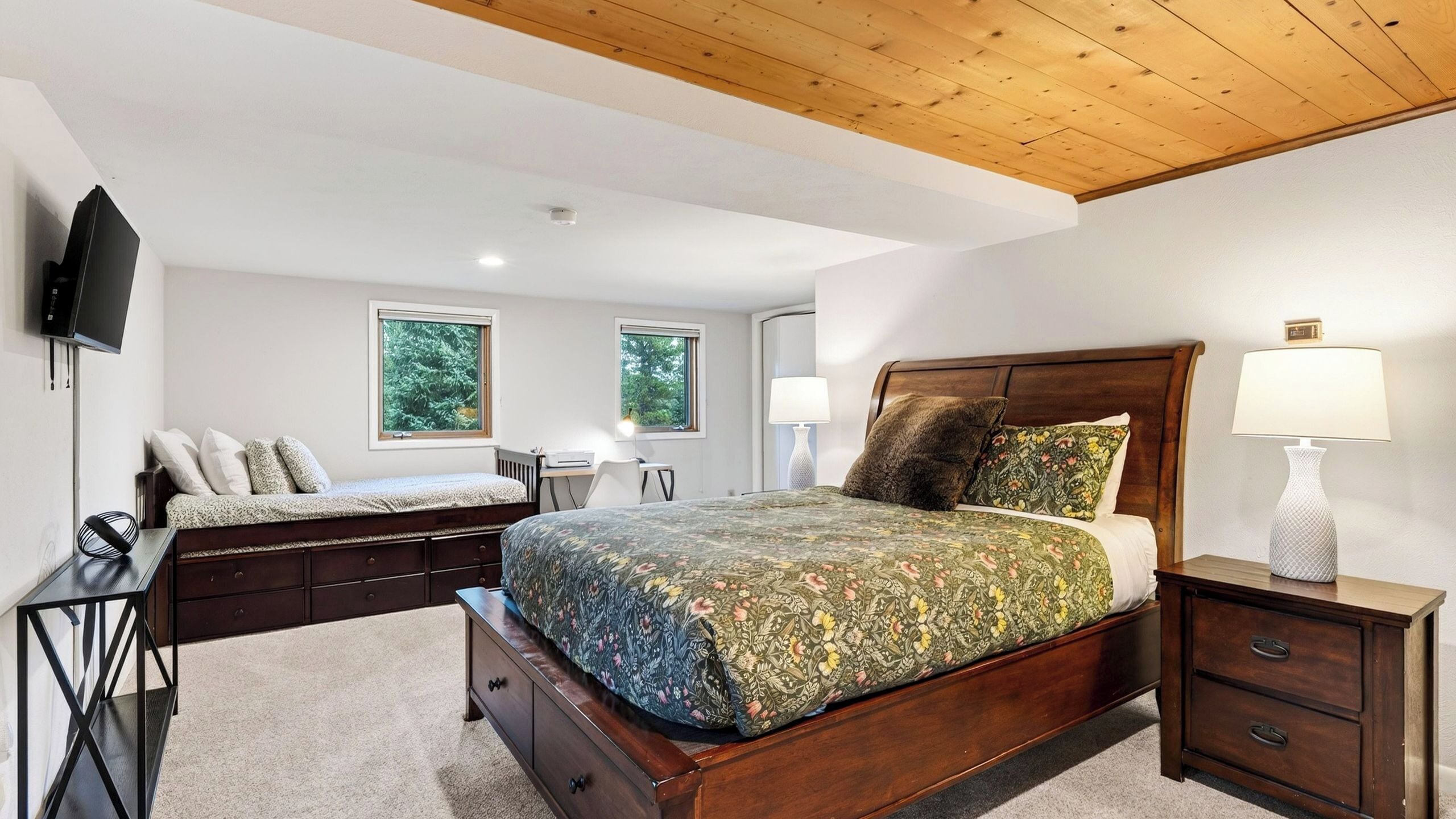 Une chambre à coucher avec un lit en bois, des tables de chevet, un bureau et un téléviseur fixé au mur.