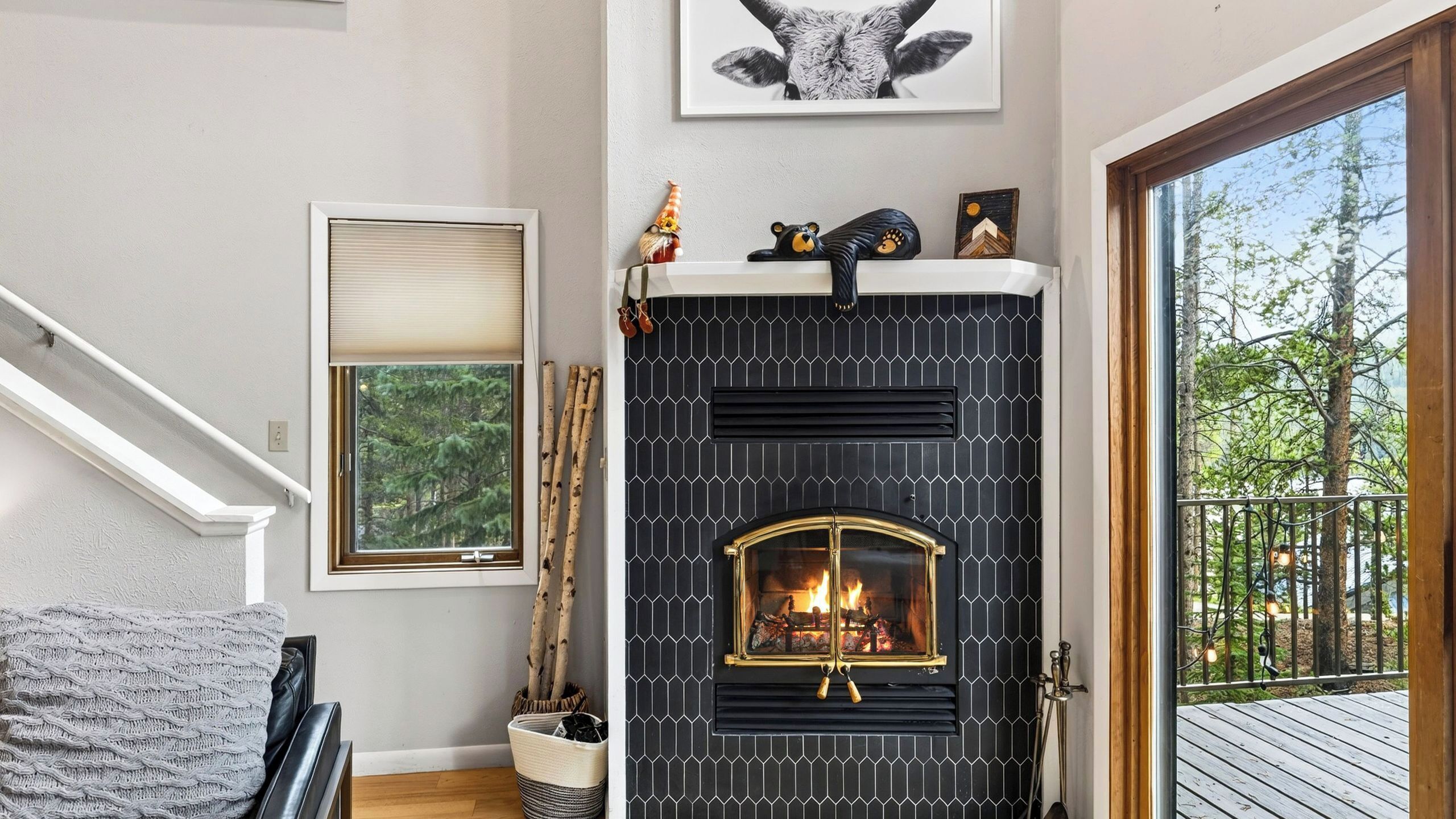 Una chimenea con un diseño de baldosas negras, un ventanal con vistas a árboles y una escalera que sube a un nivel superior.