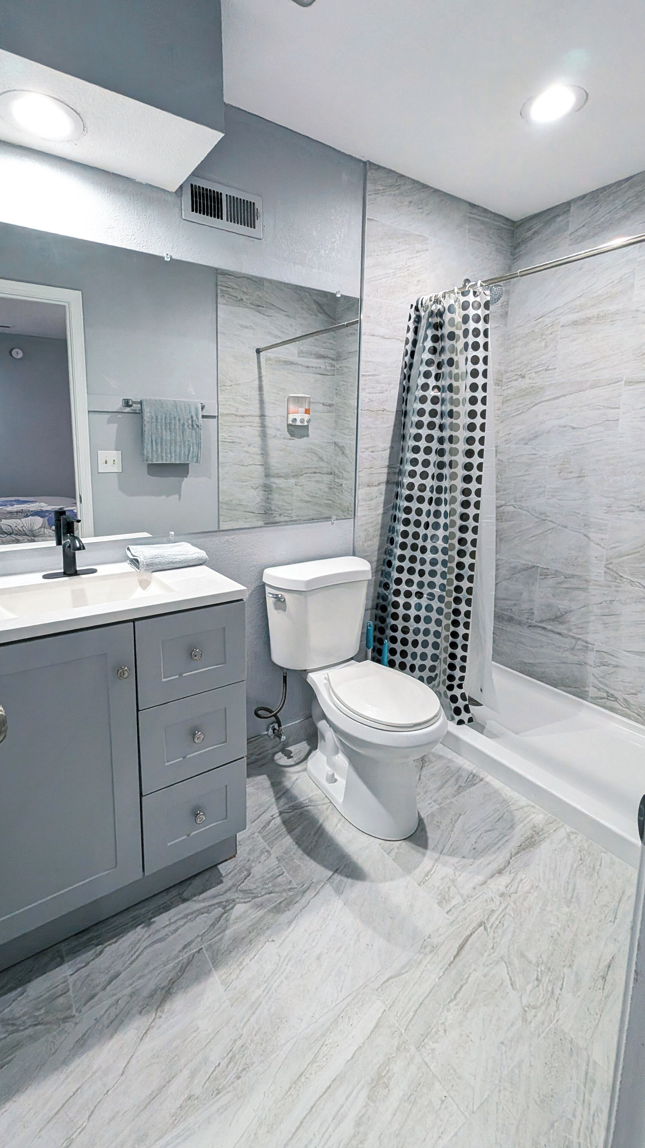 Une salle de bain moderne avec un meuble-lavabo gris, des toilettes et une douche dotée d’un rideau ajouré.