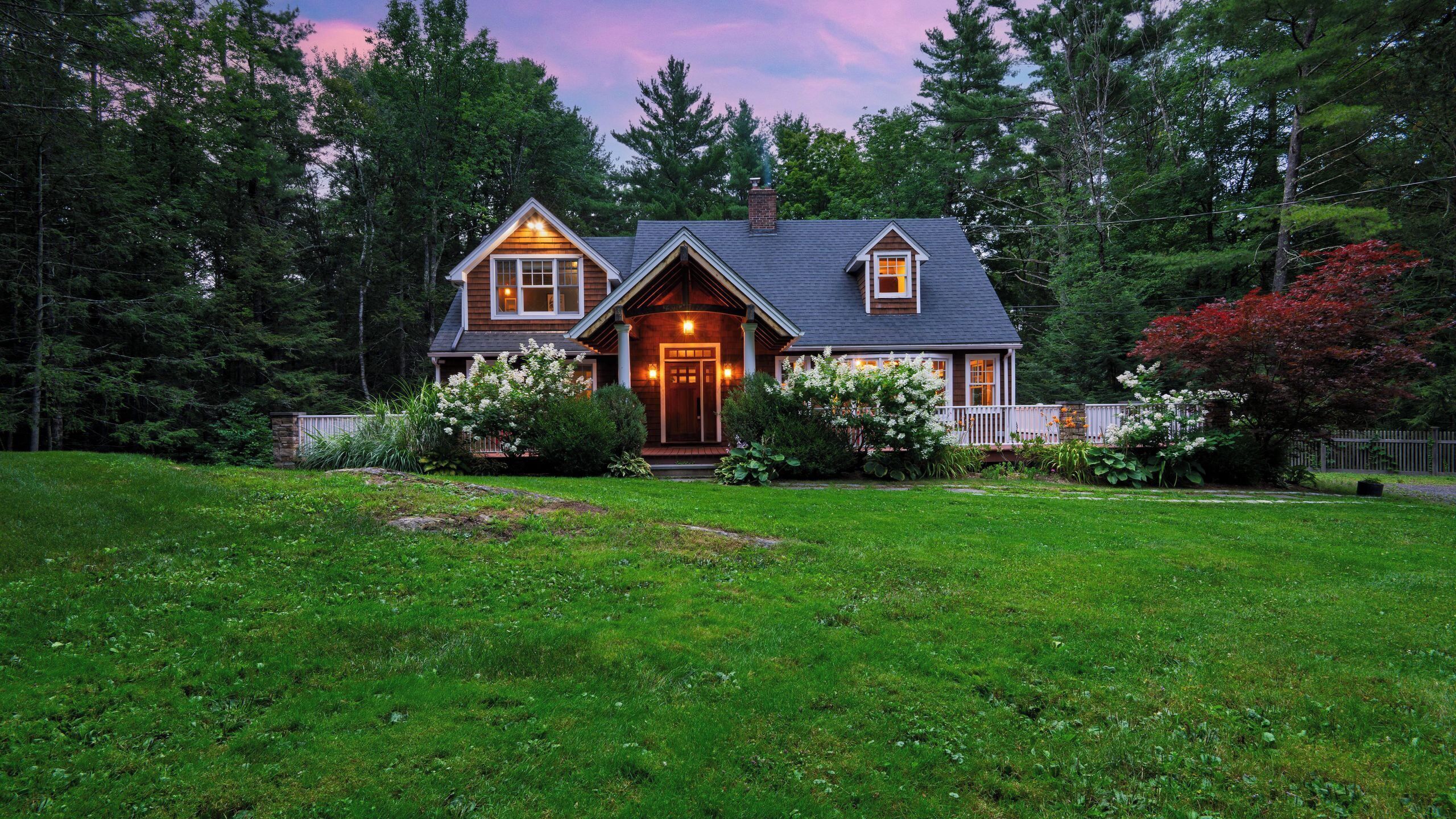 A two-story house with a front porch, surrounded by a well-maintained lawn and trees.