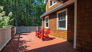 Une terrasse en bois avec une balustrade blanche, deux chaises Adirondack rouges et un pilier en pierre.