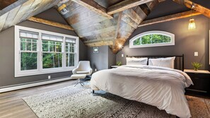 A bedroom with a large bed, a window, a chair, and a small table.