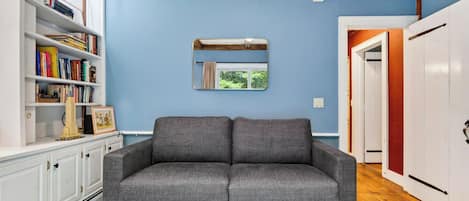 Um quarto com um sofá cinzento, uma estante de livros e um espelho na parede.
