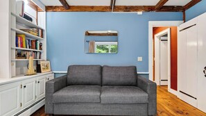 Ein Zimmer mit grauem Sofa, einem Bücherregal und einem Spiegel an der Wand.
