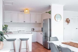 Eine moderne Küche mit weißen Schränken, einem Edelstahlkühlschrank und einer Bar mit Sitzgelegenheiten.