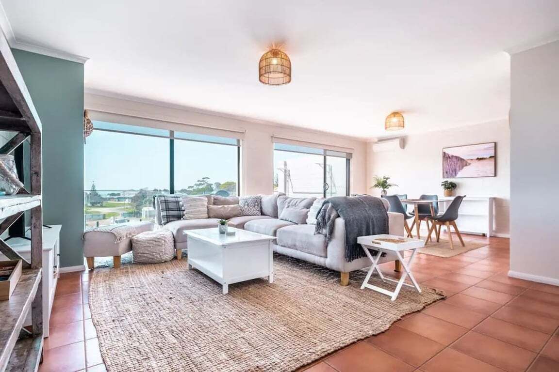 Uma sala espaçosa com uma janela grande, um conjunto de sofás, uma mesa de centro e uma área de jantar com cadeiras.
