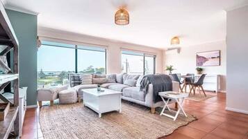 Uma sala espaçosa com uma janela grande, um conjunto de sofás, uma mesa de centro e uma área de jantar com cadeiras.