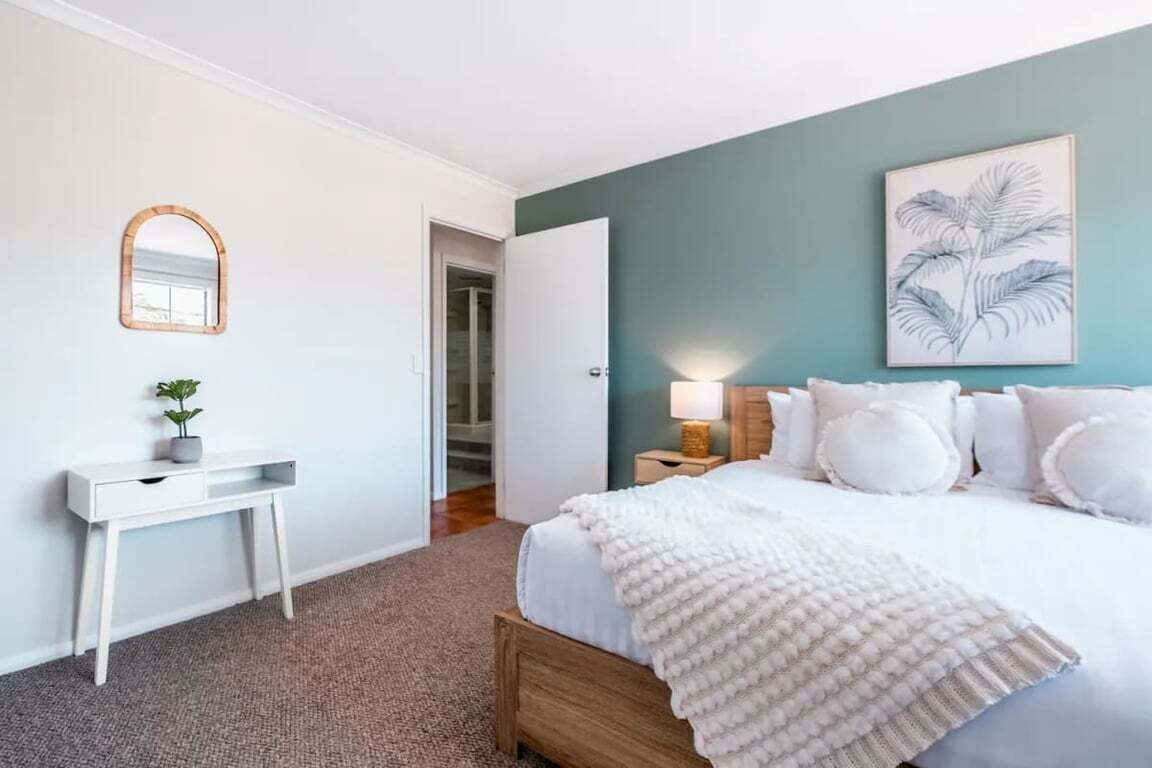 A bedroom with a bed, bedside table, and a wall-mounted mirror.