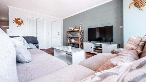 A living room with a sofa, a coffee table, a TV, and a bookshelf. - The Rooftop - Bicheno Accommodation (Bicheno)