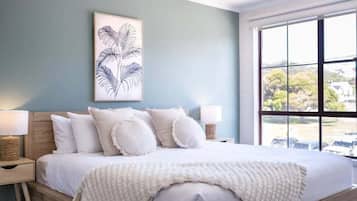 Quarto com cama, travesseiros, abajur, uma obra de arte na parede e janela com vista.