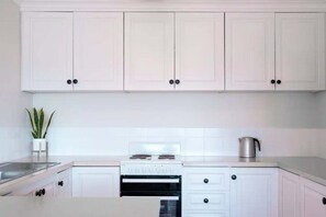 A kitchen with white cabinets, a stove, and a kettle.