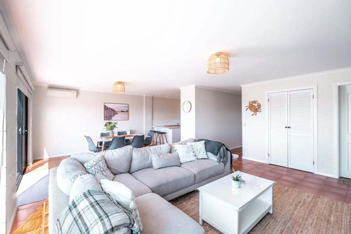 A modern living room with a sectional sofa, a coffee table, and a dining area in the background.