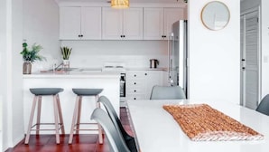 A modern kitchen with white cabinets, a central island, bar stools, and a dining table. - The Rooftop - Bicheno Accommodation (Bicheno)